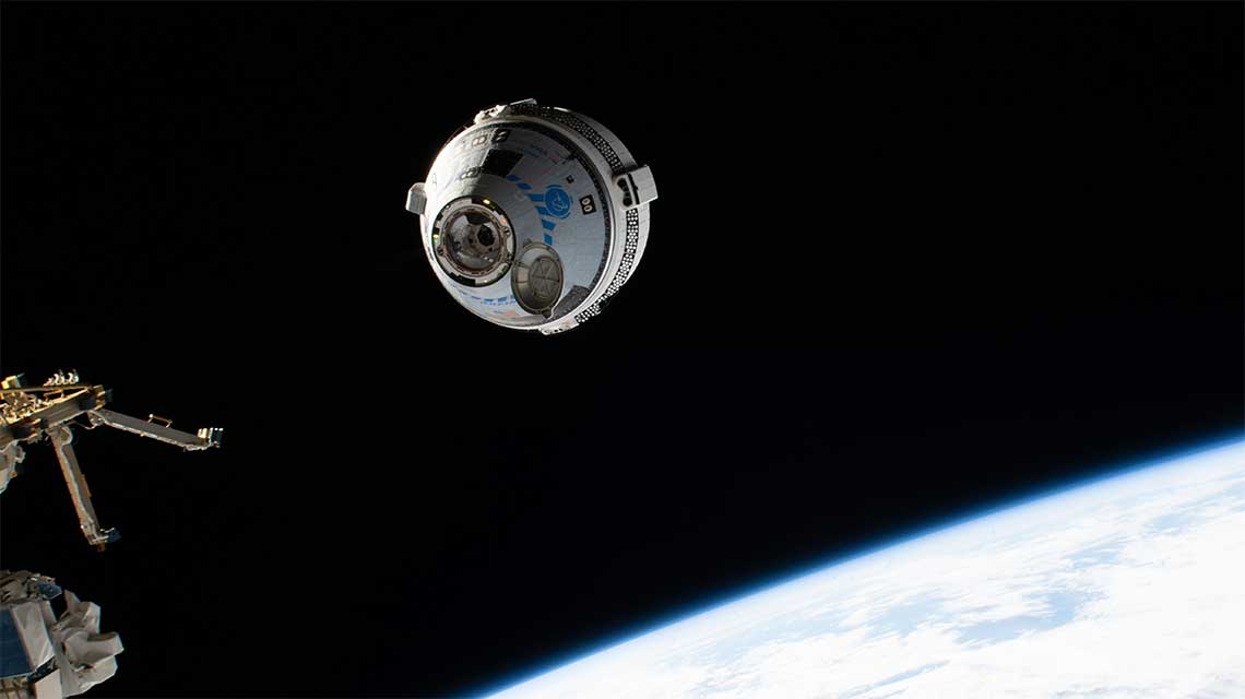 Un vaisseau spatial Starliner s'approche de la Station spatiale internationale. On voit une partie de la Terre