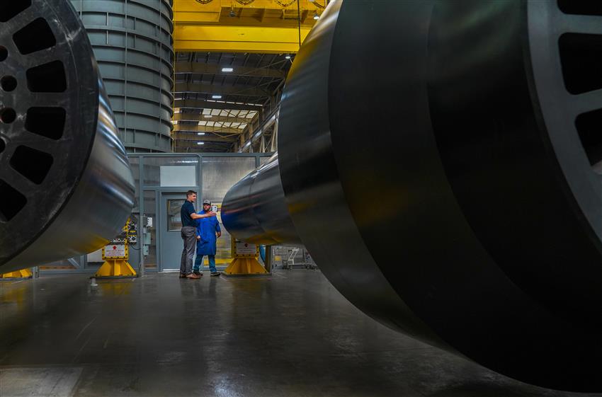 Two men standing next to very large round metal pipes.