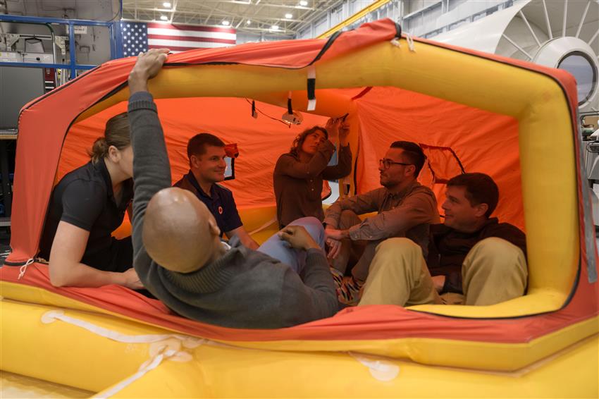 The five astronauts and an instructor sit in an inflatable boat.