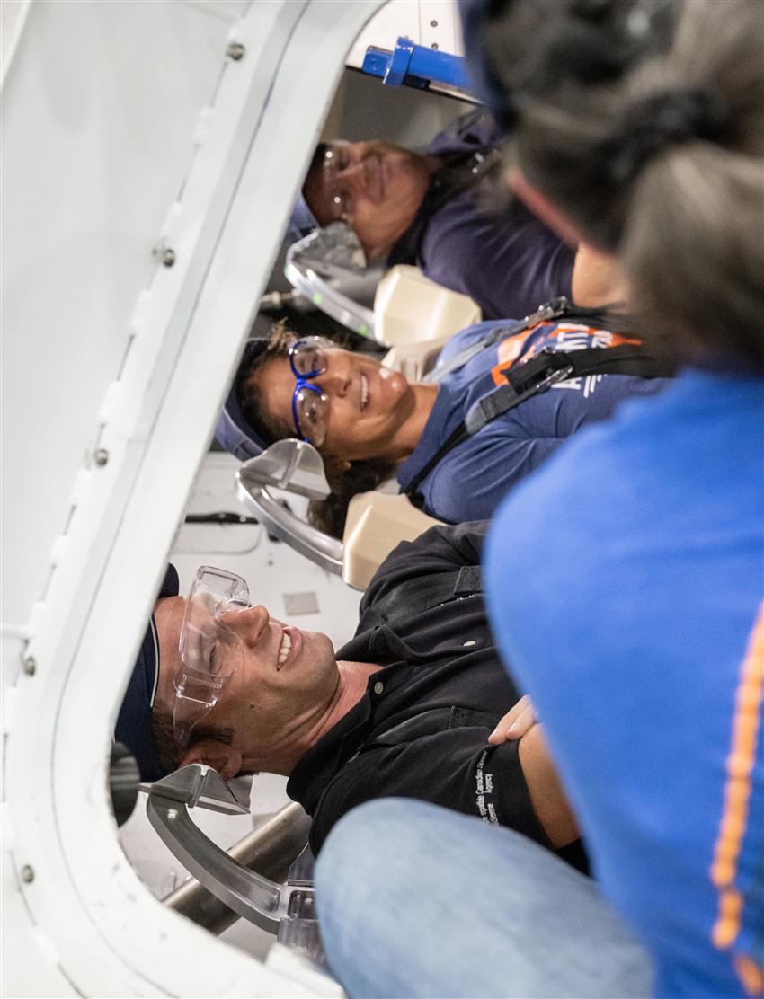 Joshua is sitting with two other astronauts in a spacecraft simulator.
