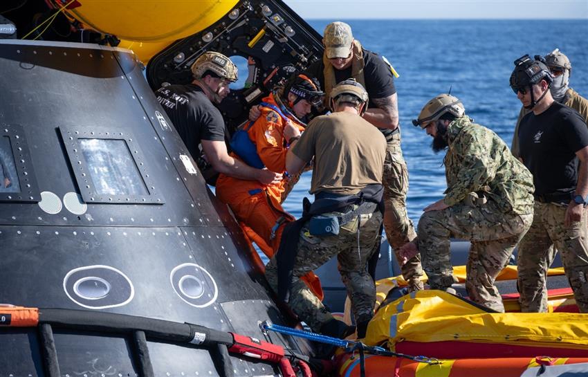 Jenni exits the Orion mockup, and some military members help her into an inflatable boat.