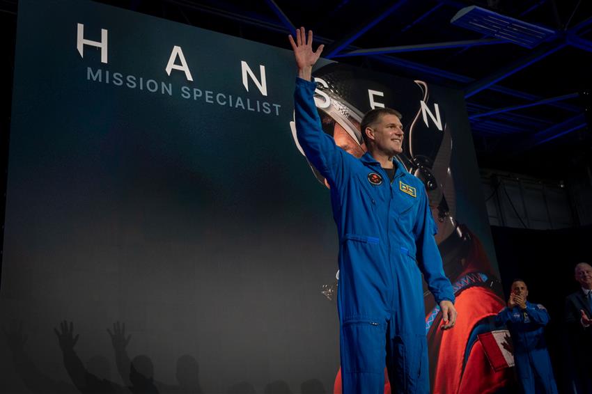 Jeremy Hansen waves to a crowd, wearing a blue flight suit