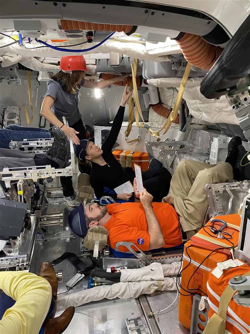 Three people working inside a spacecraft mockup.