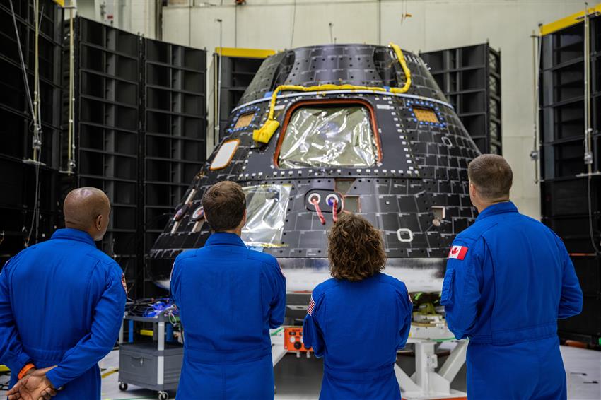 Quatre astronautes vêtus de combinaisons de vol bleues regardent une capsule.