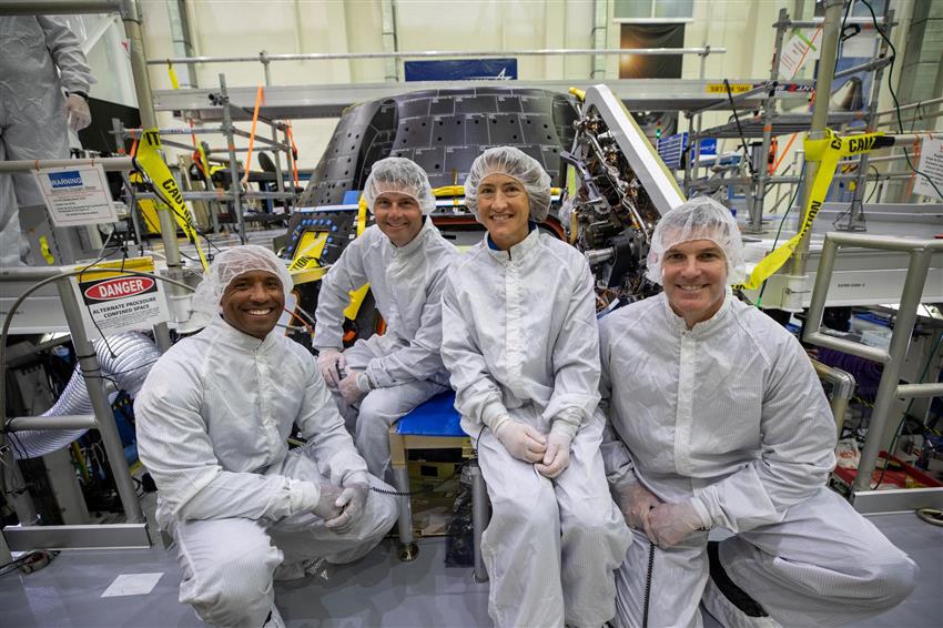 Quatre astronautes vêtus de combinaisons de protection blanches posent devant une capsule.