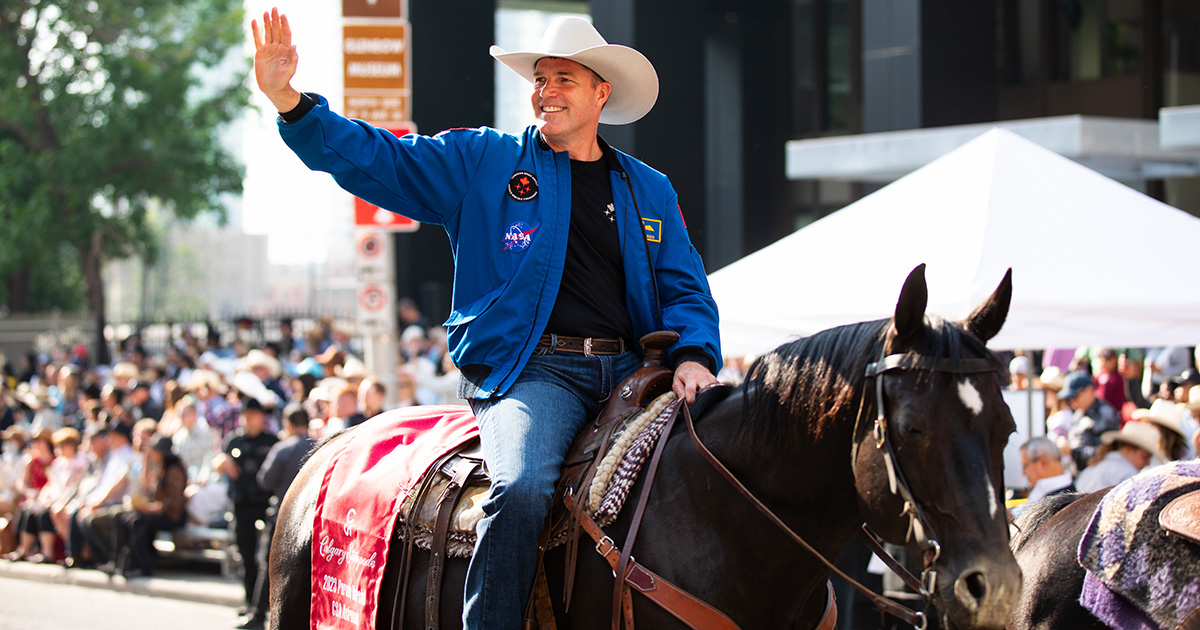 Jeremy Hansen waves to families gathered along a street as he rides a horse