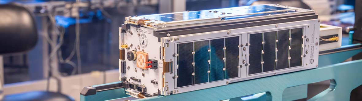 Gros plan d'un CubeSat doté de panneaux solaires sur un support dans un laboratoire.