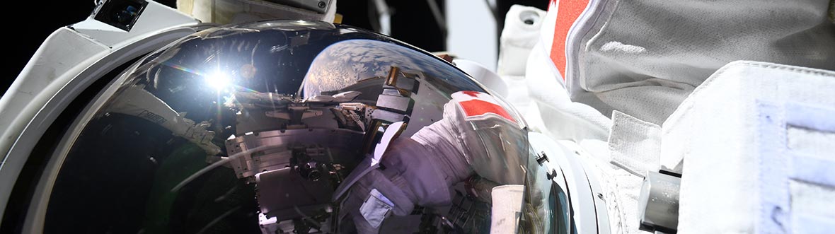 Joshua Kutryk in his space suit, outside the International Space Station. The end of the Canadarm and Earth are visible behind him.