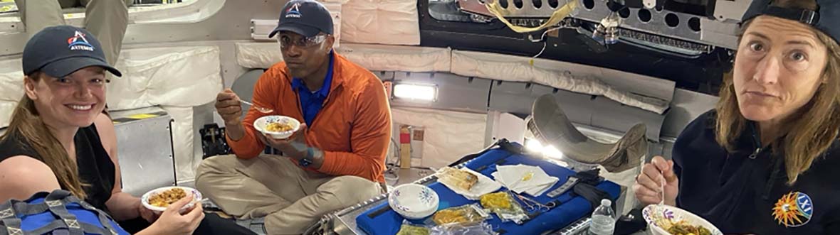 Jenni Gibbons, Reid Wiseman, et Christina Koch mangent de la nourriture spatiale dans une maquette d'Orion. (Source : NASA)
