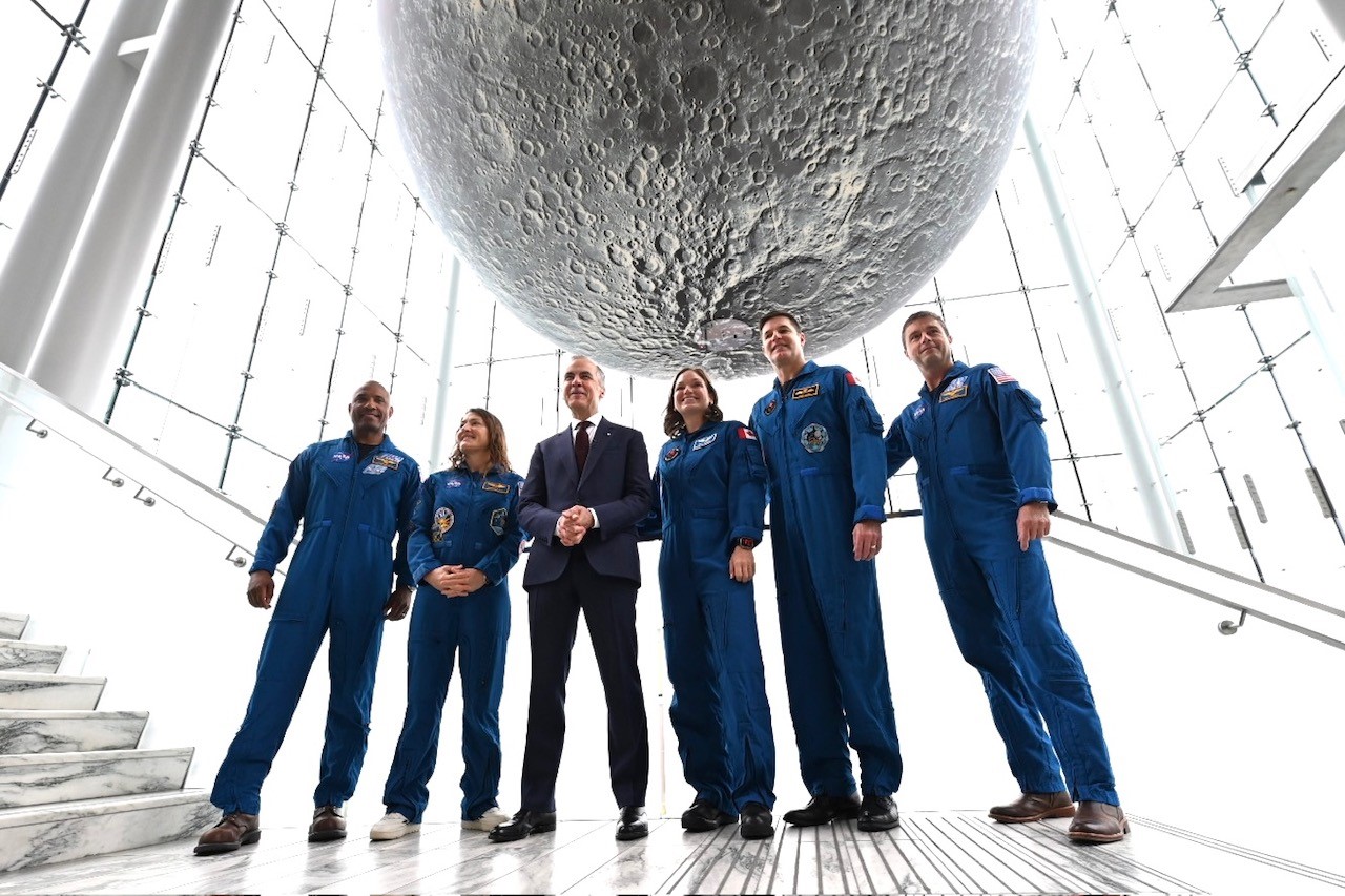 The five astronauts and the Prime Minister, with a big Moon globe above them.
