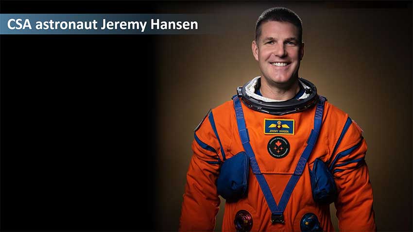Astronaut Jeremy Hansen standing and smiling. He is wearing an orange space suit