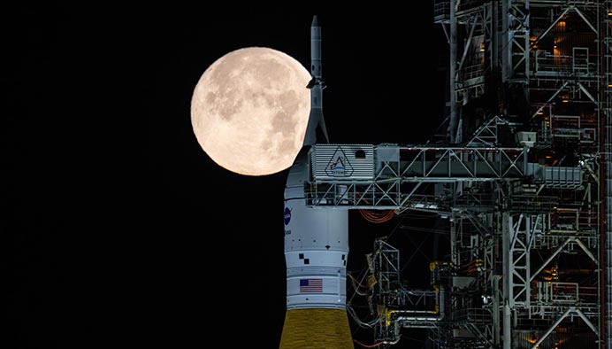 Close-up of the top part of the SLS rocket, with the full Moon shining in the night sky.