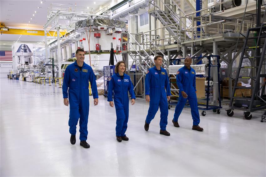 Four astronauts walk side by side in a NASA assembly facility.