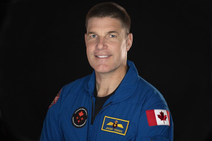 A portrait of Jeremy Hansen, he is facing the camera and wearing a blue flight suit