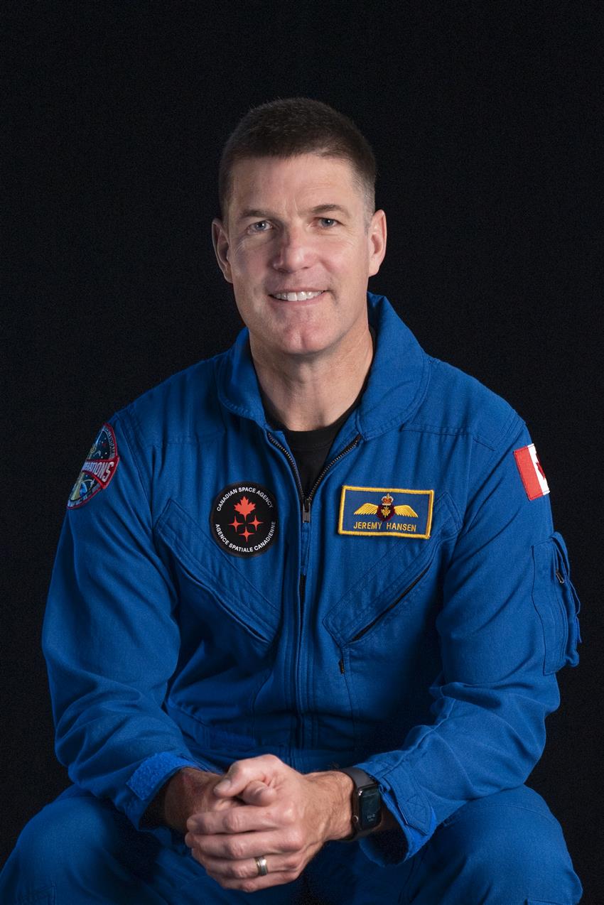 Jeremy Hansen sits facing the camera, he is wearing a blue flight suit