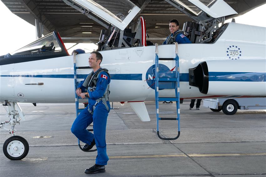 Joshua stands next to an airplane while Jessica sits inside it. 