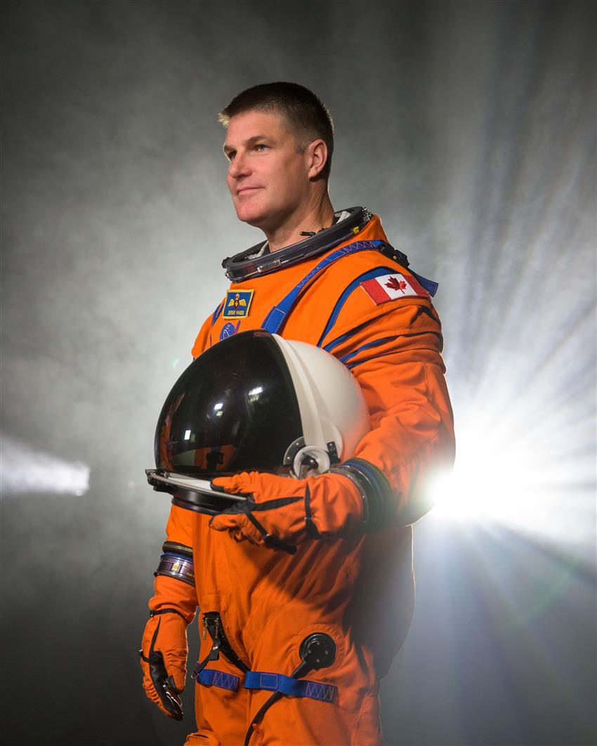 Plan américain de l'astronaute Jeremy Hansen, de profil, vêtu de sa combinaison de vol orange d'Artemis II