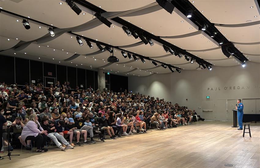 Jeremy stands in front of a seated audience, holding a microphone.