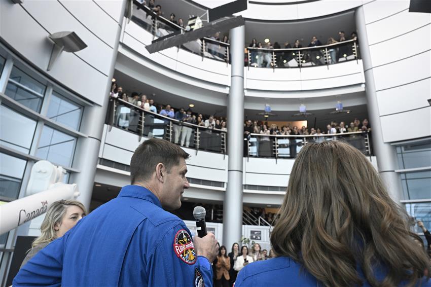 Minister Joly, Jeremy and Christina are seen from behind. Dozens of people are assembled on three floors in front of them.