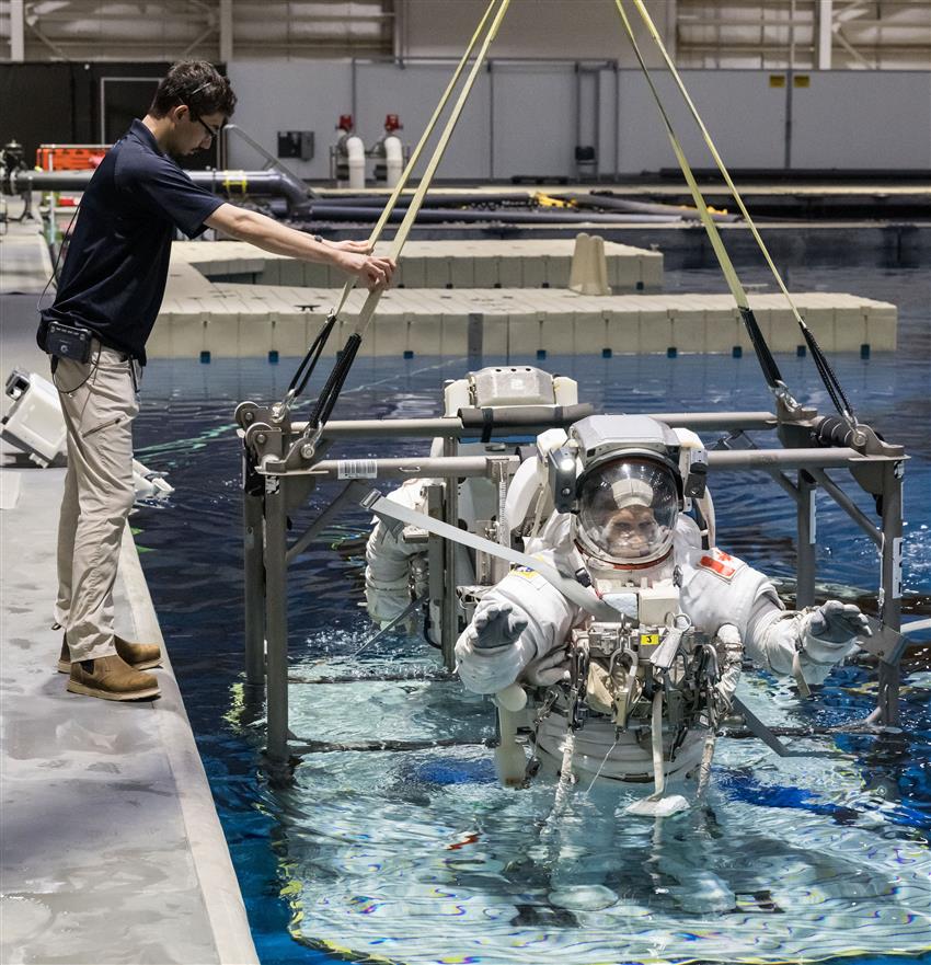 Joshua vêtu d'une combinaison spatiale, la moitié du corps immergée dans une piscine.