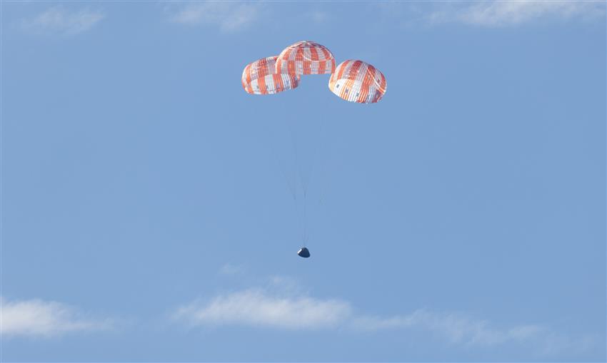 Une capsule spatiale suspendue à trois grands parachutes.