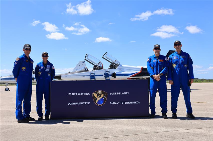 The astronauts stand on either side of a banner.