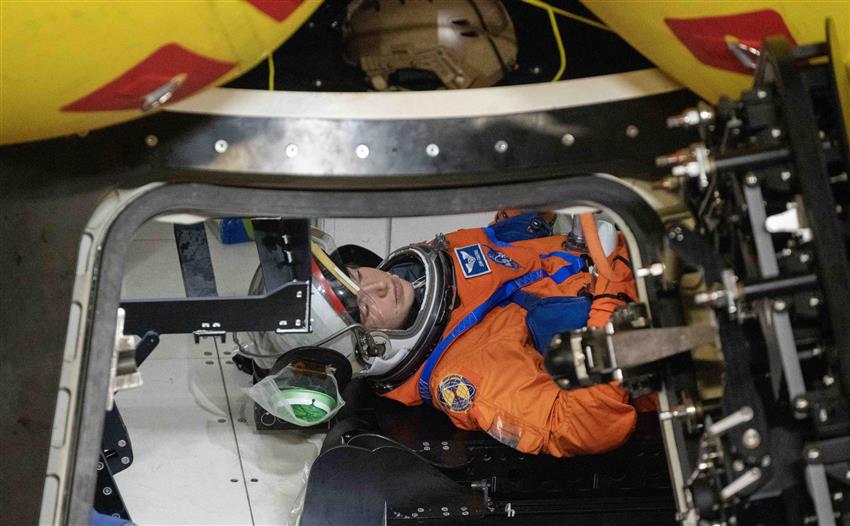Jenni attachée avec une ceinture dans la maquette d'Orion, en attente de sortir de la capsule.