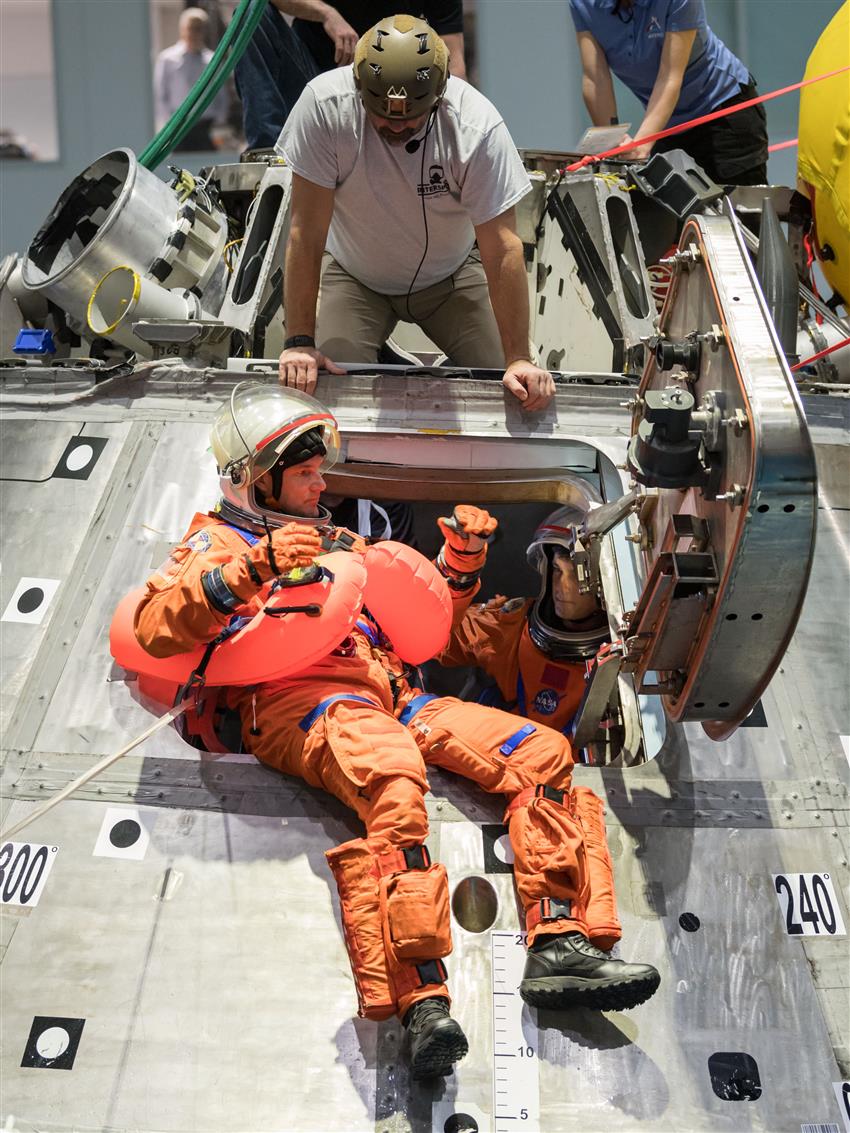 Jeremy, wearing a spacesuit, evacuates a model space capsule during an exercise.