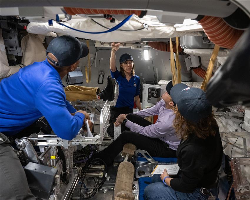 Four people inside a spacecraft mockup.