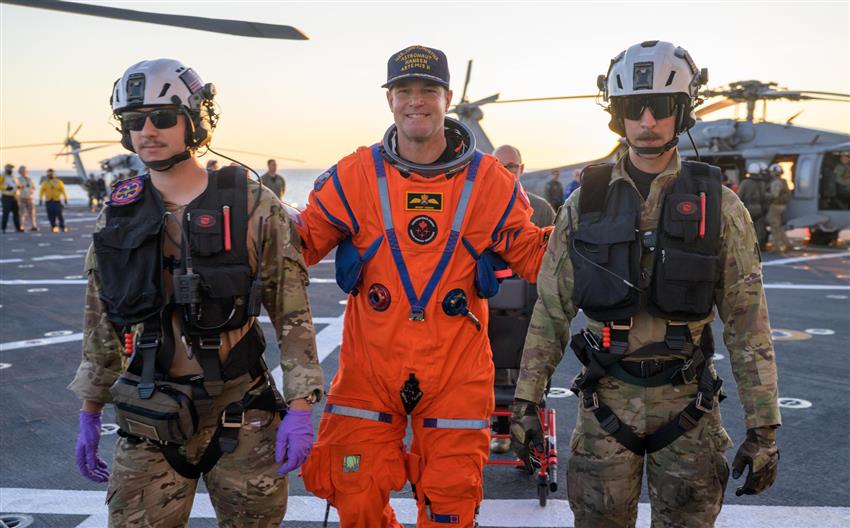 Jeremy vêtu de sa combinaison spatiale entre deux membres de l'équipe de récupération. 