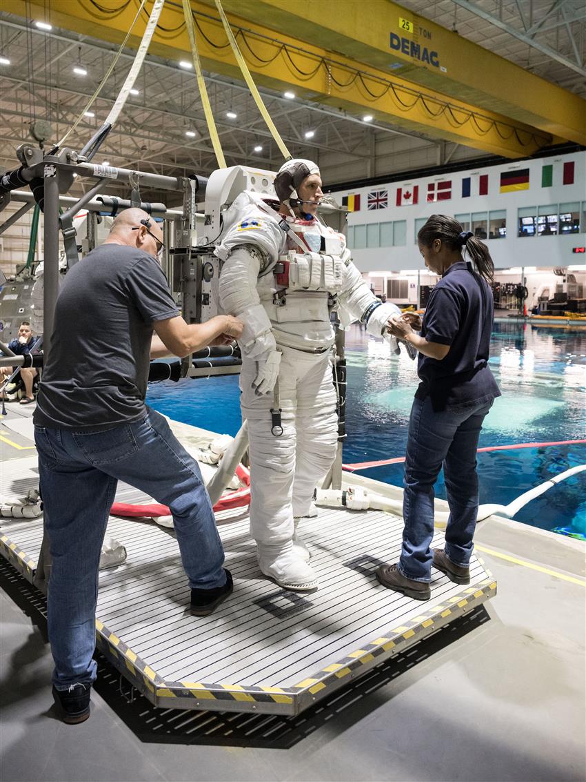 Deux techniciens aident Joshua à mettre sa combinaison spatiale.