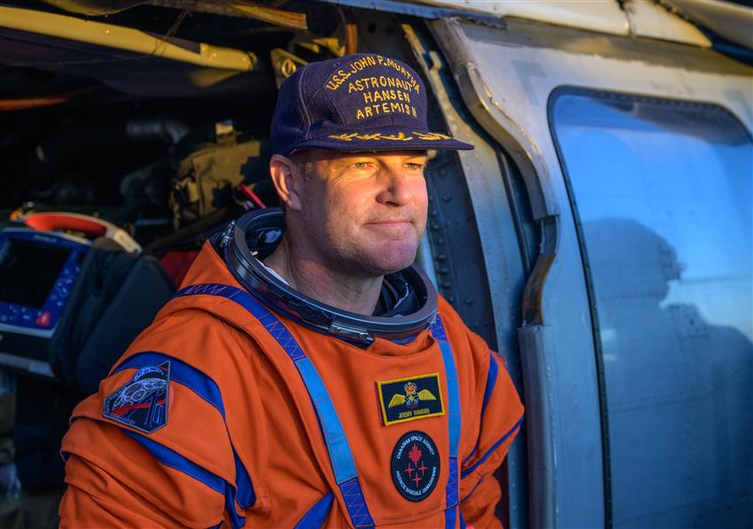 Jeremy vêtu de sa combinaison spatiale, assis sur le bord d'un hélicoptère. 