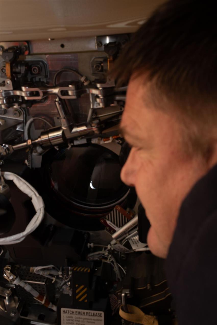 Close-up of Jeremy's face looking through one of Orion's windows back at Earth. 