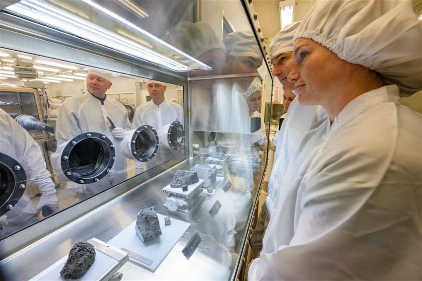 Jenni Sidey-Gibbons, Jeremy Hansen and other people stand in front of a glass case holding samples of lunar rocks