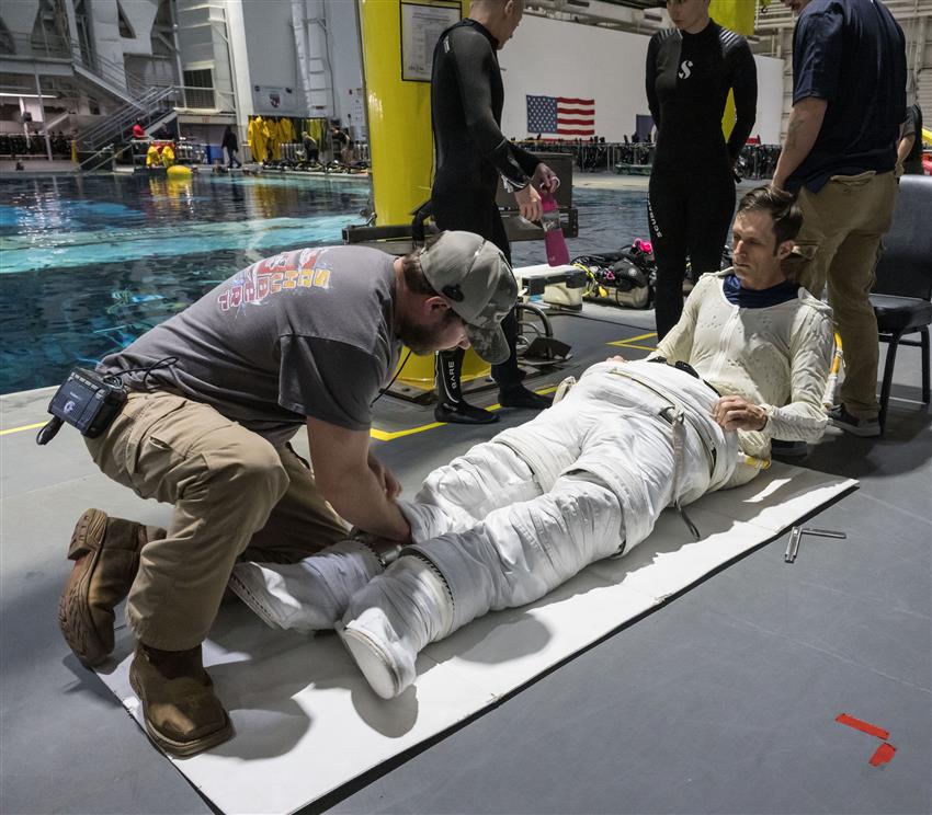 Joshua met ses jambes dans une combinaison spatiale avec l'aide d'un technicien.
