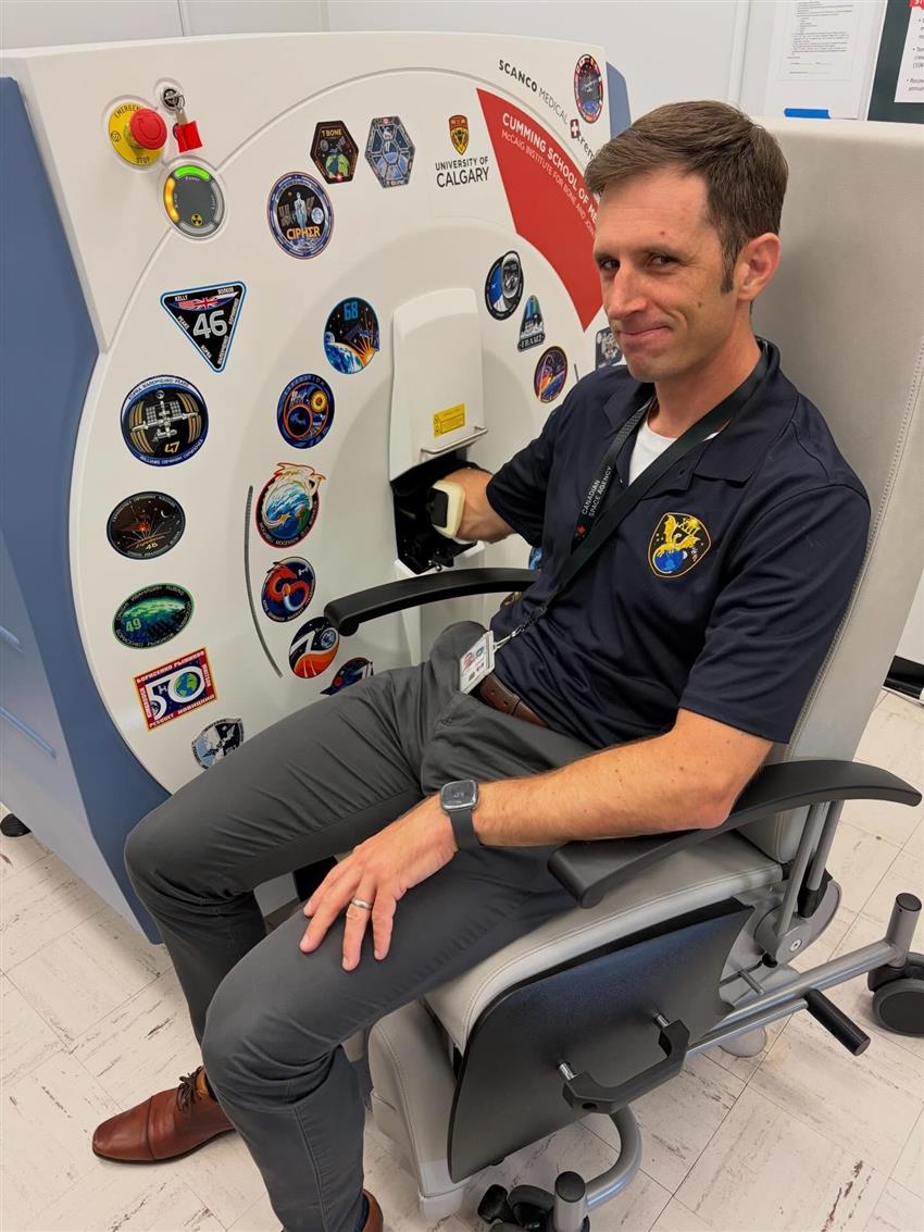 Joshua sits in a chair with his right arm placed in a large scanning machine. 