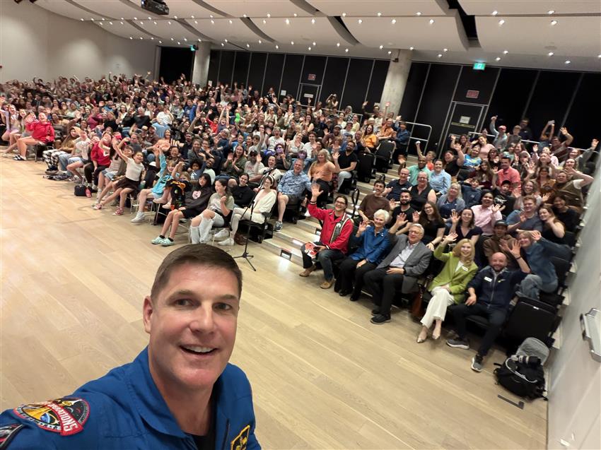 Jeremy takes a selfie with a crowd sitting behind him.