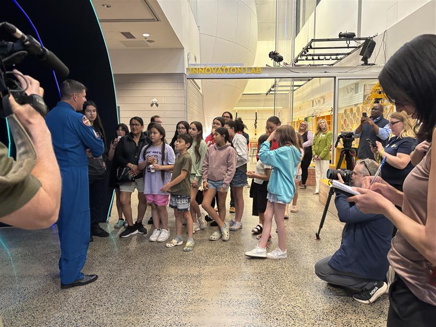 Jeremy stands in front of a group of students. Media and science centre representatives look on.