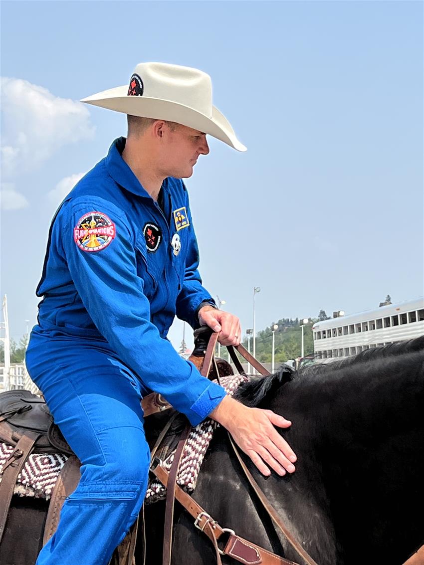 Jeremy Hansen, in a blue flight suit and cowboy hat, riding a black horse