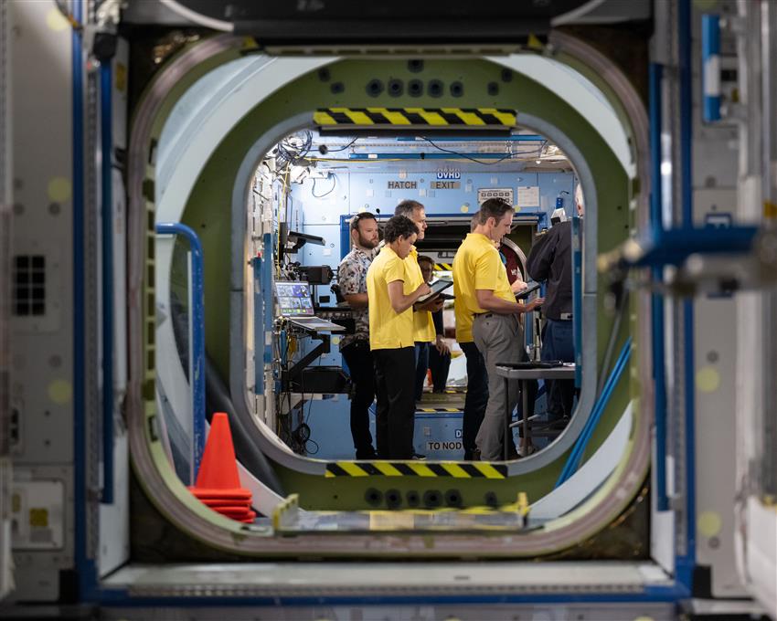 Jessica, Luke, Joshua and Sergey look at screens inside a mock-up of the International Space Station. 