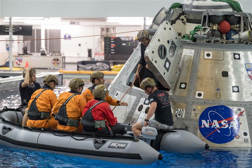L'équipage de Crew-13 et des techniciens sur un radeau gonflable près d'une capsule spatiale dans une piscine.