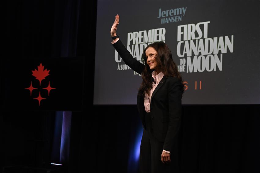 Lisa Campbell waves her hand as she stands in front of a big screen.