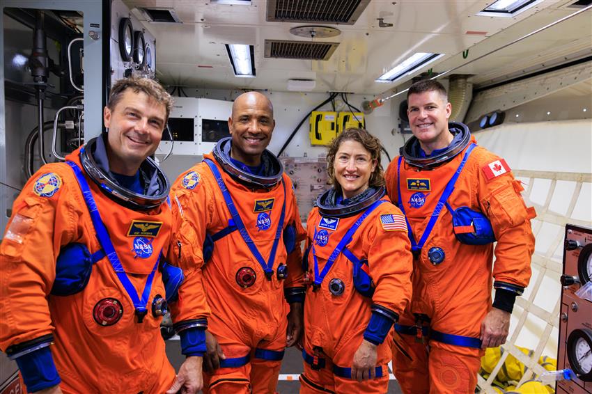 Four astronauts wearing orange spacesuits.