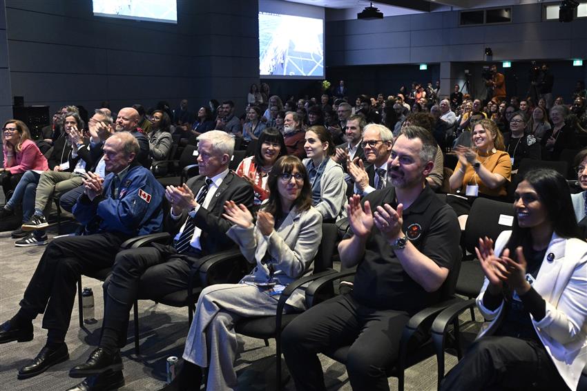 Une centaine de personnes applaudissent dans une salle de conférence. 