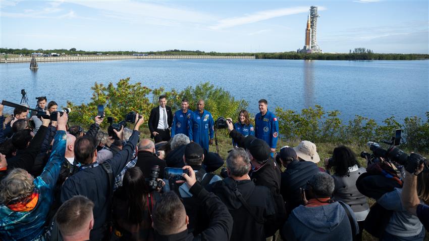 L'équipage d'Artemis II et Jared devant de nombreux journalistes. À l'arrière-plan, le lanceur SLS.
