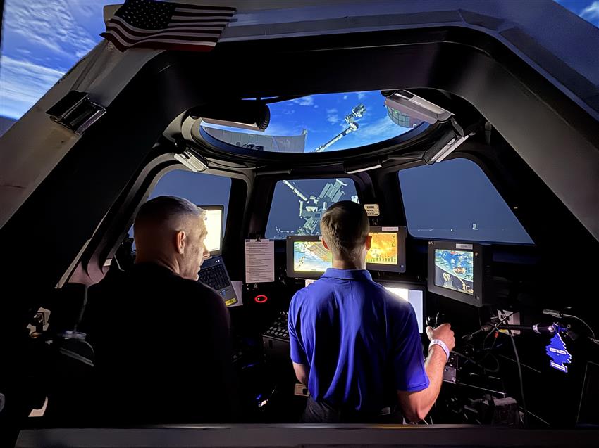 Joshua utilise les commandes du simulateur tandis que Luke regarde par-dessus son épaule.