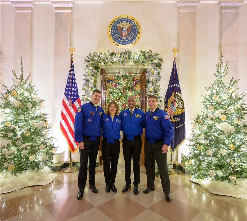 The four astronauts standing in a room decorated for Christmas.