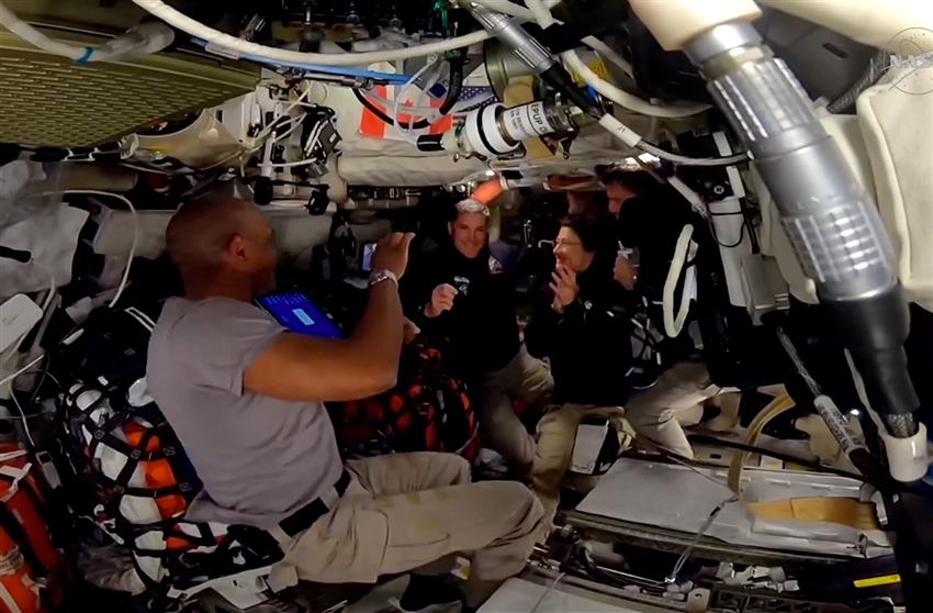 Victor, Jeremy, Christina and Reid inside the Orion spacecraft, smiling and clapping while Jeremy holds his gold wings. 