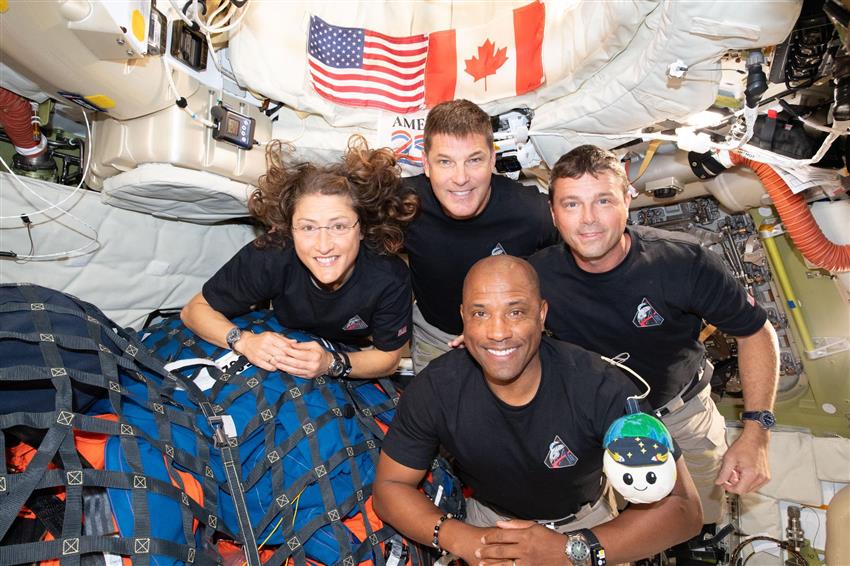 Christina, Jeremy, Reid, and Victor pose for a photo in the Orion capsule with a plush Moon.