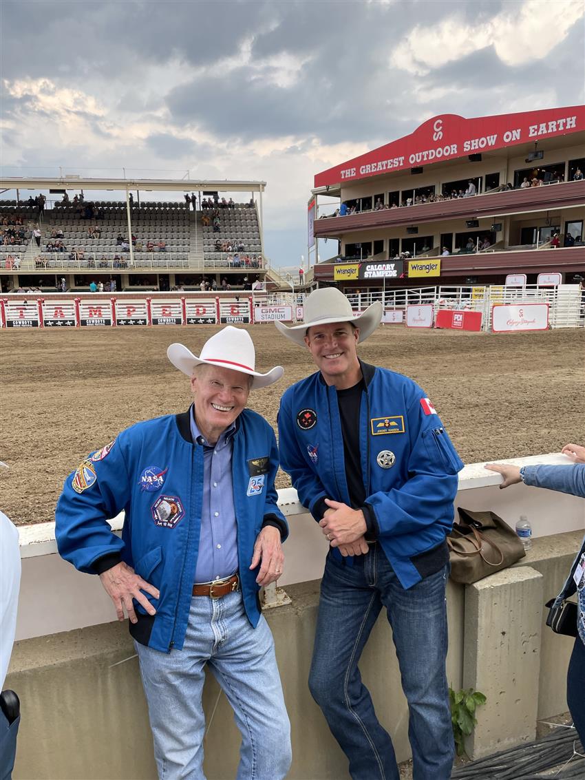 Bill Nelson (left) and Jeremy Hansen lean on a palisade, rodeo grounds behind them
